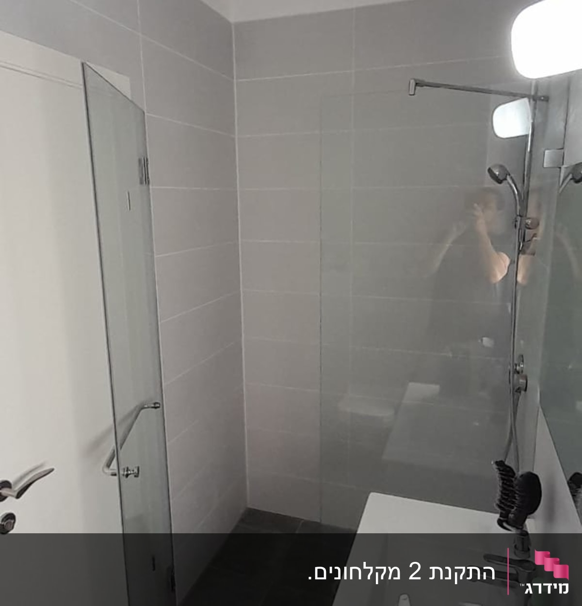 מקלחון זכוכית עם ראש מקלחת על קיר אריחים אפורים